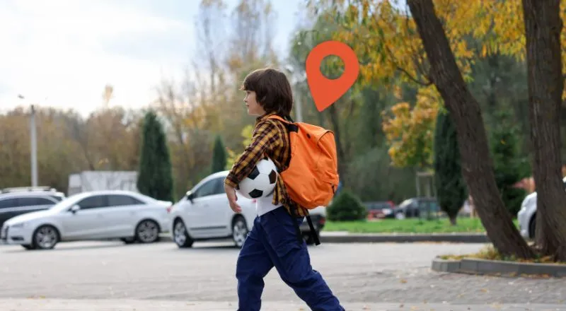 A child walking through a car park with an orange backpack and an orange location pin hovering over him.