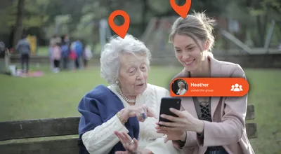 An elderly woman and her adult daughter looking at the Device Tracker Plus app together on a park bench