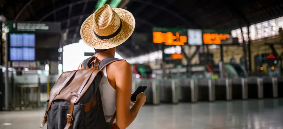 Solo female traveller with a backpack and sun hat checking her phone in a train station