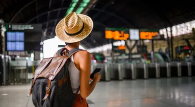 Solo female traveller with a backpack and sun hat checking her phone in a train station